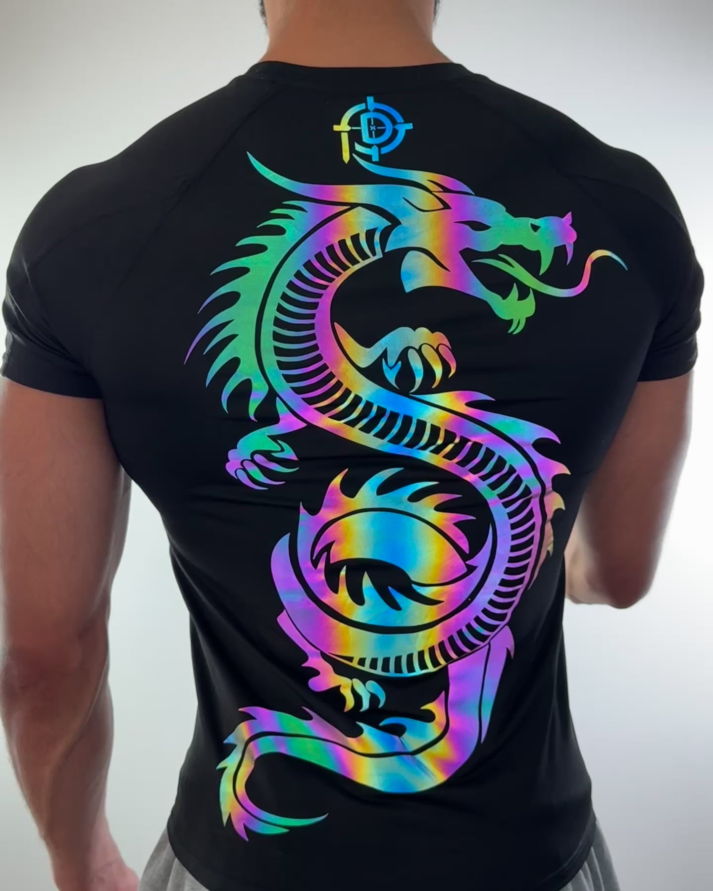 Video of a man wearing a black compression shirt with a large iridescent dragon design glowing under light on the back