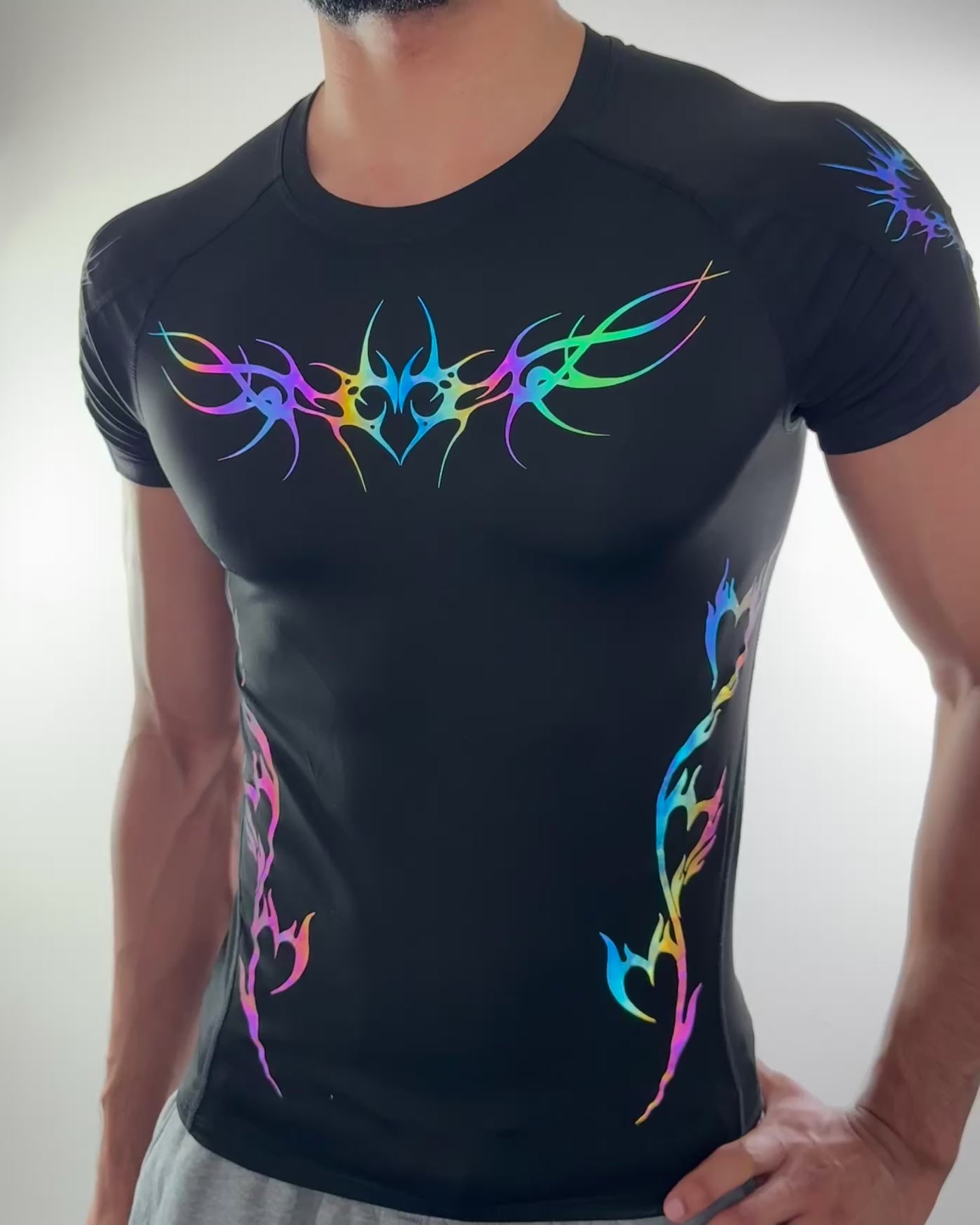Men’s fitted black compression shirt with rainbow reflective tribal heart and flame designs across chest and sides. Model moving to show reflection effect.