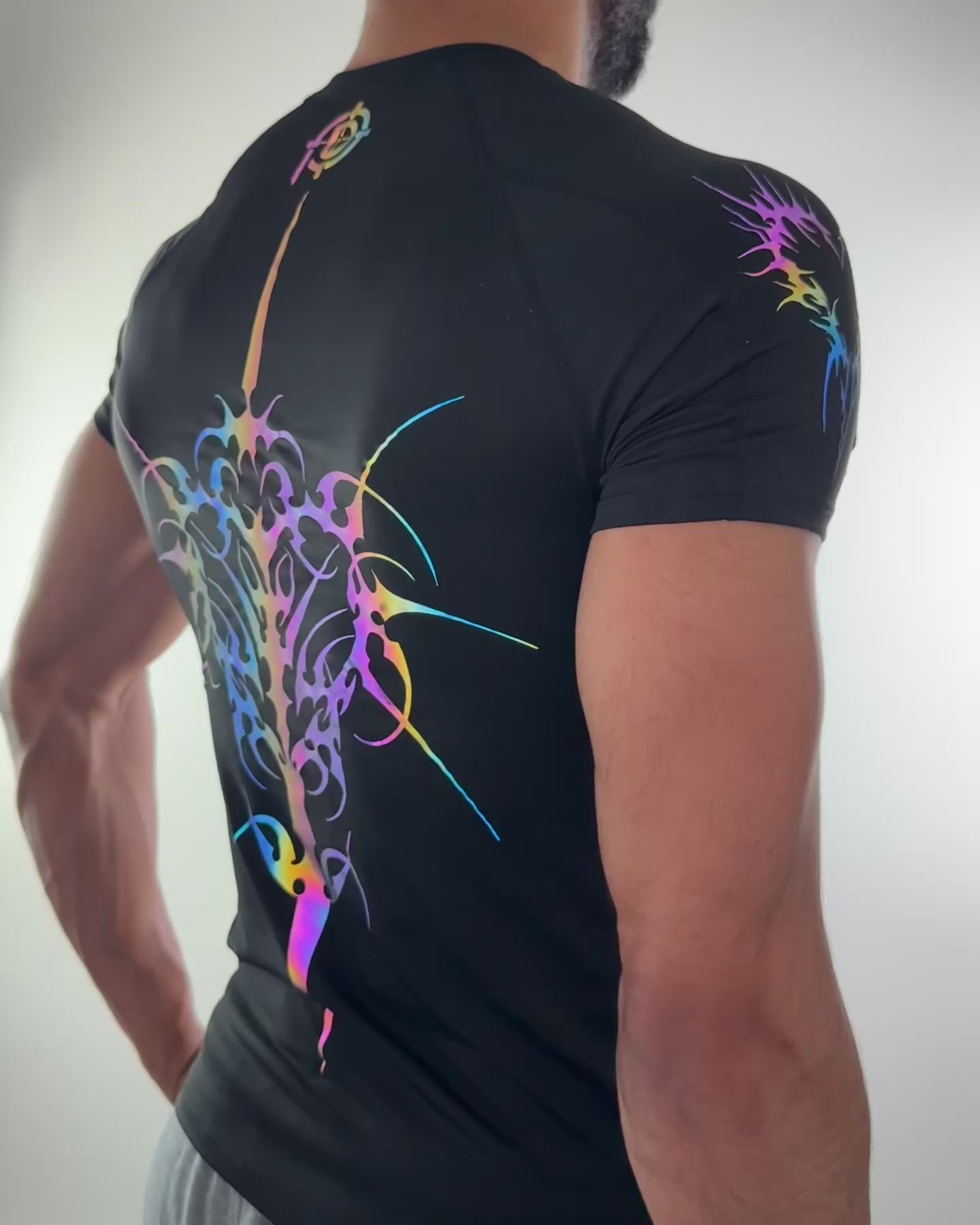 Men’s fitted black compression shirt from back view. With rainbow reflective tribal spine sword. Model moving to show reflection effect.